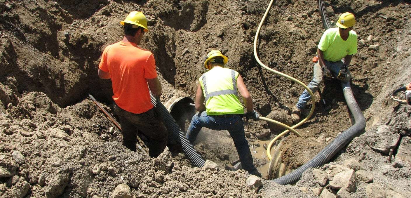 Crew in hard hats working in an excavated trench around buried pipe