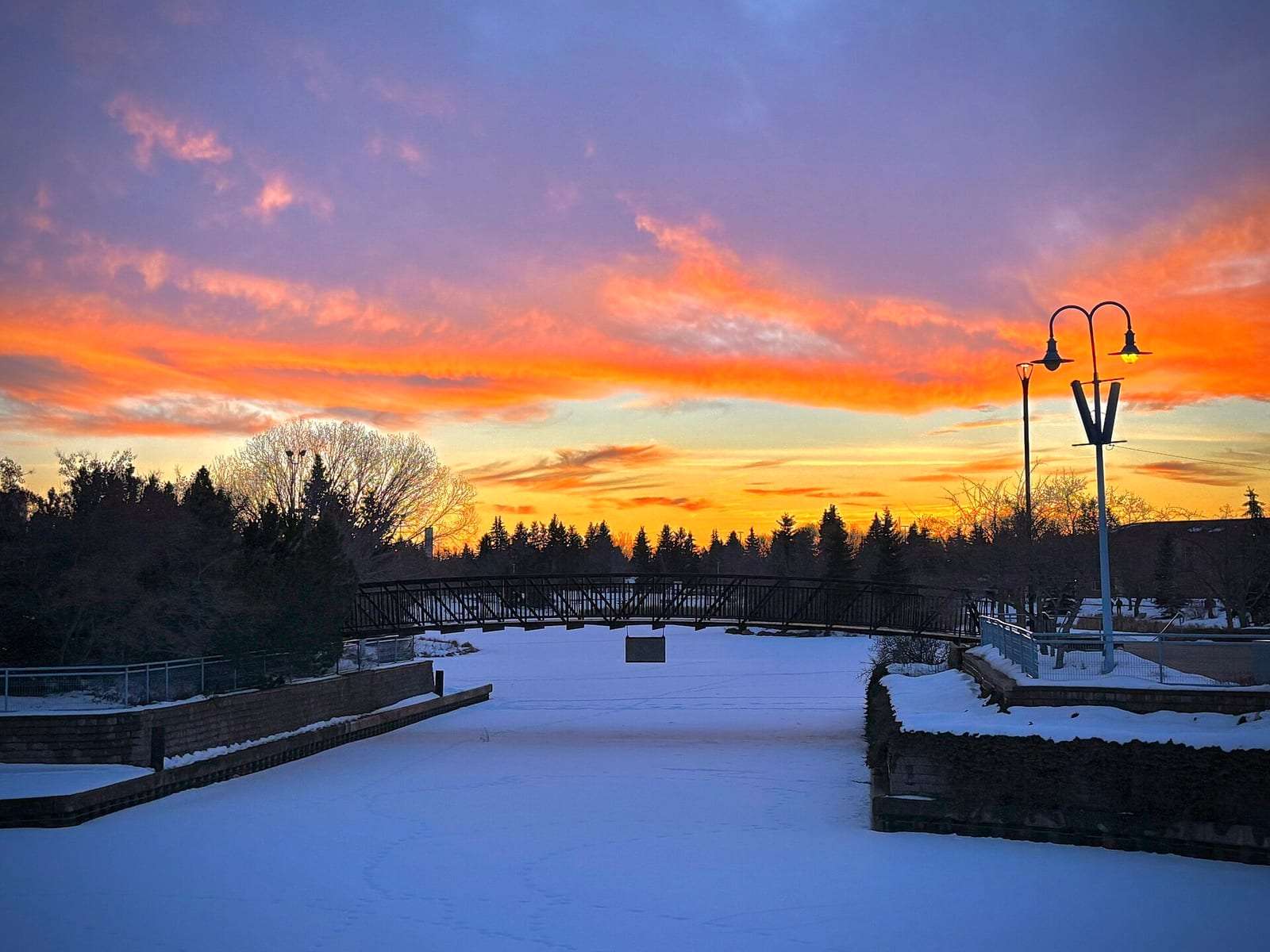 Winter sunset over a snow-covered pond and footbridge in Sherwood Park, Alberta
